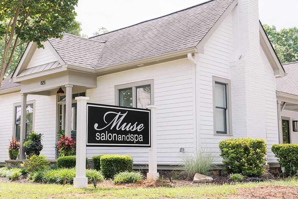 White house with "Muse Salon and Spa" sign, surrounded by greenery and flowers.