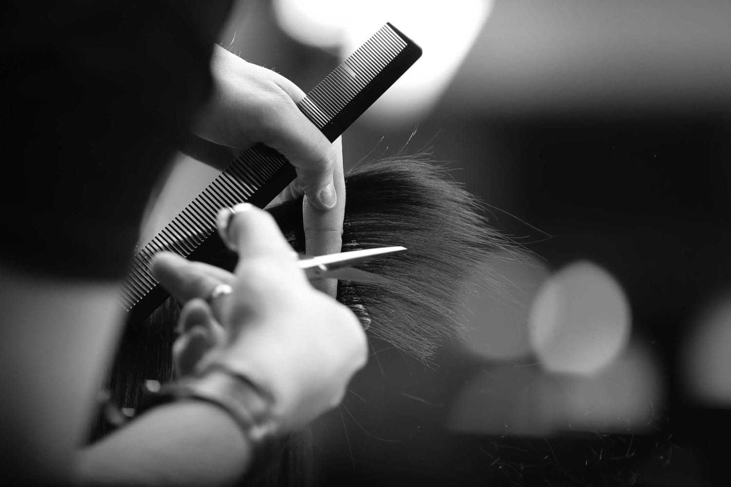 Hairdresser cutting hair with scissors and comb in black and white.