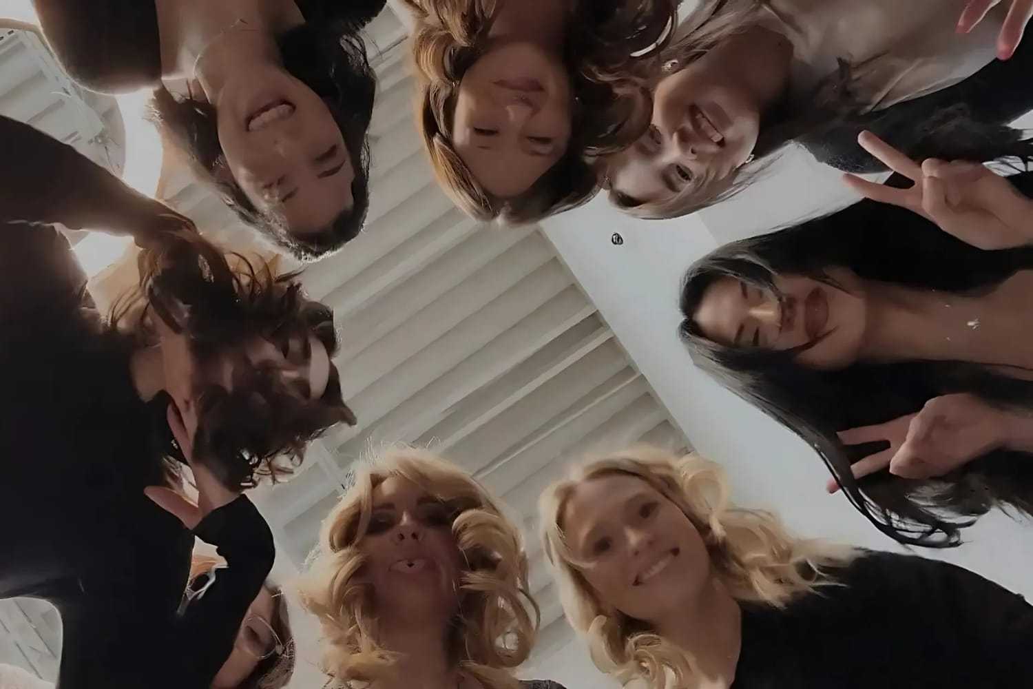 Group of friends in a circle, smiling down at camera.